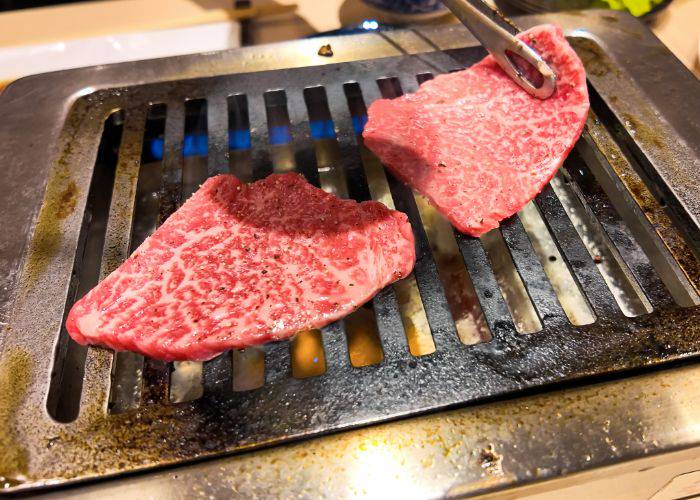 A slice of wagyu beef being flipped at a yakiniku restaurant.